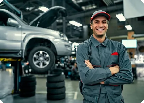 A technician standing in front of a vehicle on a lift in a busy service bay